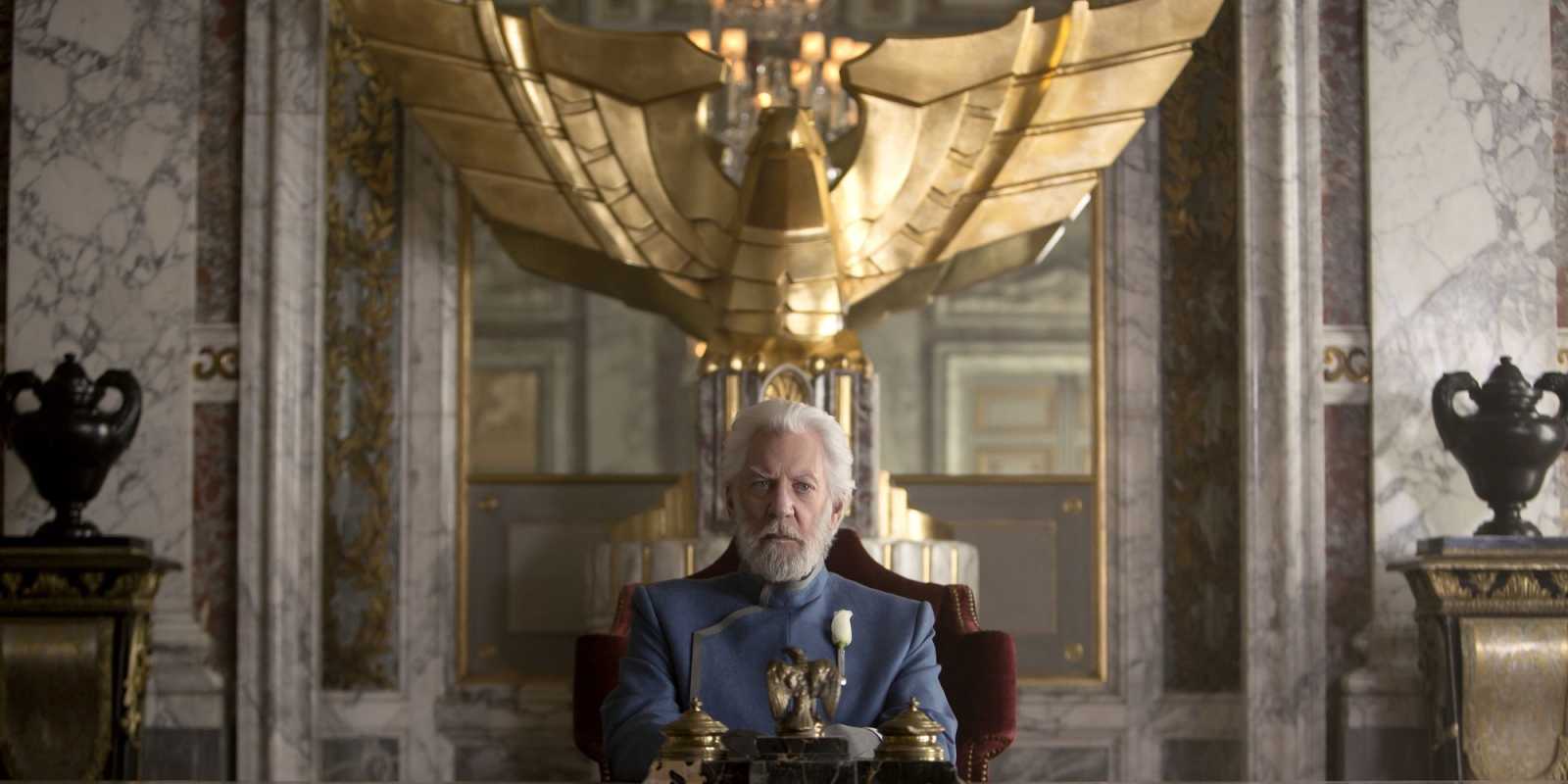 El presidente Coriolanus Snow se sienta en una mesa con una gran estatua de águila dorada detrás de él en Sinsajo