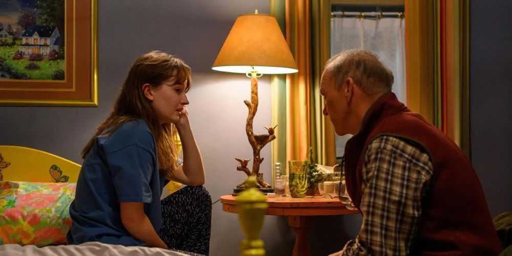 Kaitlyn Dever ako Betsy Mallum sedí na posteli vo svojej spálni oproti Michaelovi Keatonovi ako Dr. Samuel Finnix vo filme Dopesick